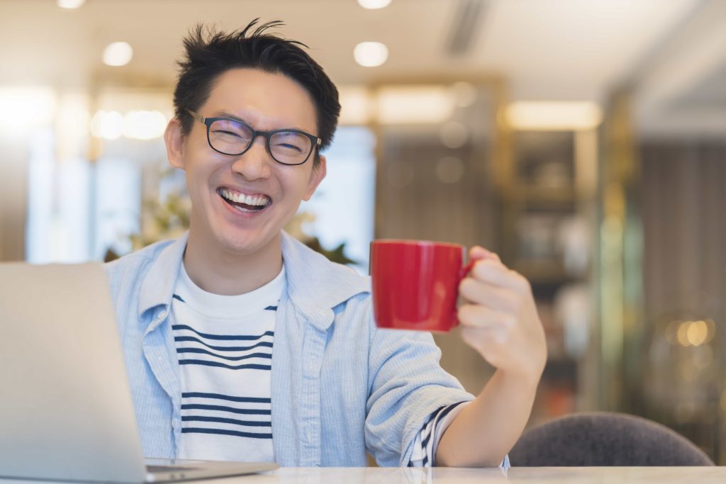 Young man with a bright smile enjoying a coffee, showcasing confident, well-designed teeth